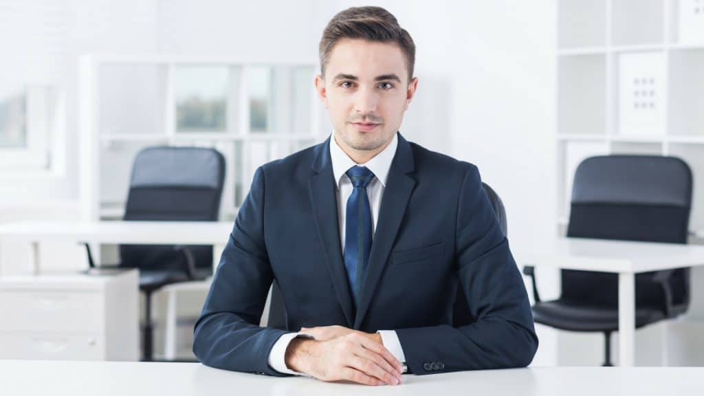 Geschäftsmann im Anzug mit blauer Krawatte am Verhandlungstisch sitzend