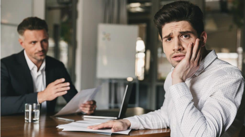 Unternehmer schaut überfordert in die Kamera während Berater ihm etwas erklärt