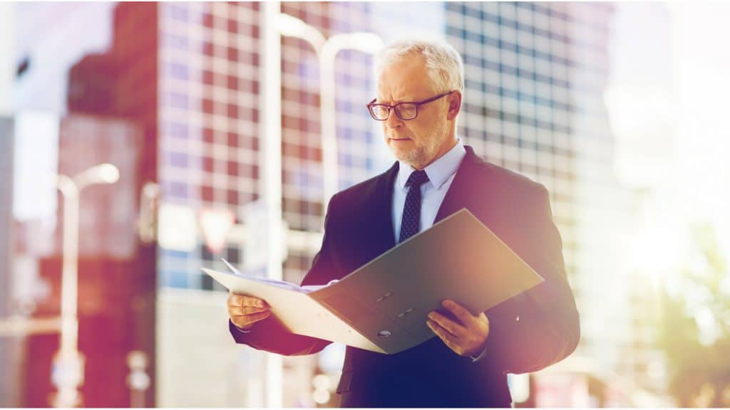 Geschäftsmann schaut auf eine geöffnete Mappe mit Papieren