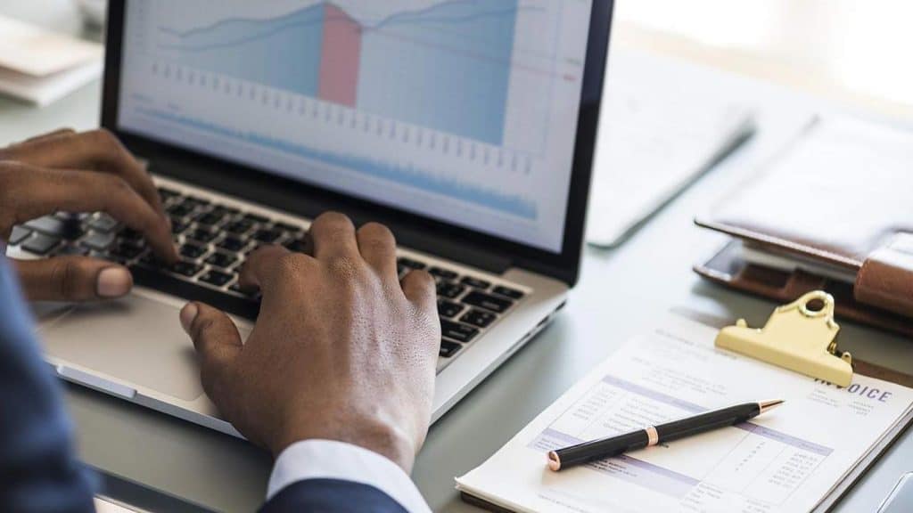 Ein Mann erstellt am Laptop ein Balkendiagramm. Neben ihm liegen Stift & Block