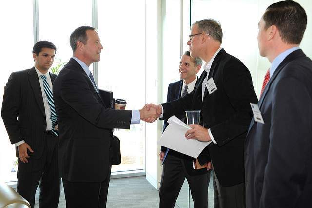 Unternehmer treffen sich in einem Raum & schütteln sich zur Begrüßung die Hand