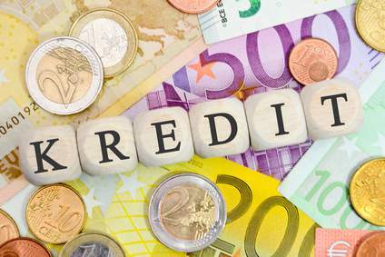 Ein Tisch voller Bargeld mit dem Wort Kredit auf Holzmurmeln darauf