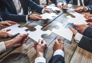 Geschäftsleute an einem Tisch halten Puzzleteile aus weißem Papier zueinander
