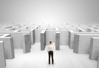 Mann steht vor einem weißen Betonlabyrinth und greift sich verwundert an den Kopf