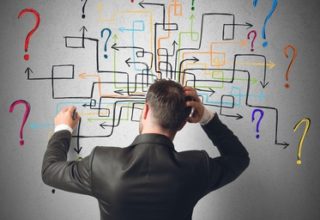 Mann im Anzug zeichnet Plan aus bunten Pfeilen und kratzt sich fragend am Kopf.