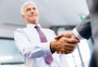 Ein Berater schüttelt einem Kunden die Hand und lächelt dabei