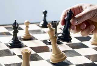 Schachbrett mit Schachfiguren, bei dem eine schwarze Figur die Königin schlägt.