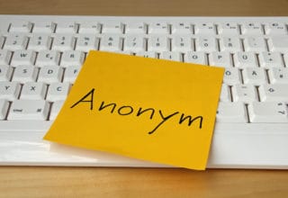 Eine weiße Tastatur mit einem orangenem Klebezettel darauf: Anonym