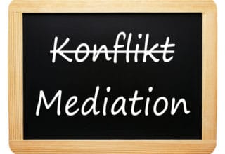 Eine Schiefertafel mit Wort Konflikt durchgestrichen & Mediation darunter stehend