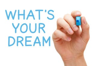 Hand schreibt mit blauem Marker an eine Scheibe: What´s your Dream?
