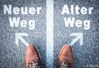 Ein Mann steht an einer Weggabelung mit der Aufschrift: Alter Weg - Neuer Weg