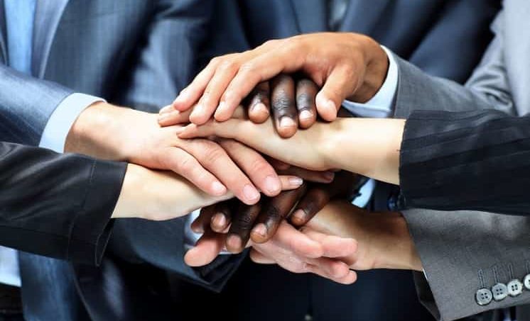 5 Menschen die Ihre Hände in der Mitte übereinander legen und eine Genossenschaft gründen