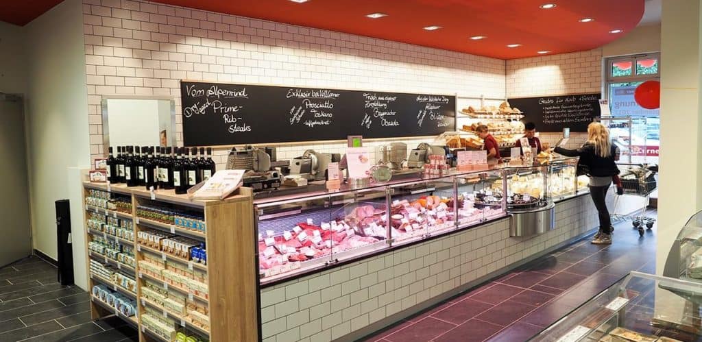 Ein Verkaufstresen im Supermarkt der mit Aufschnitt und Käse. Eine Kundin steht davor.