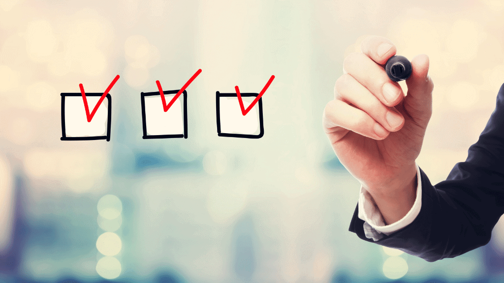 Eine Hand mit Stift die in drei Kästchen rote Haken gesetzt hat.