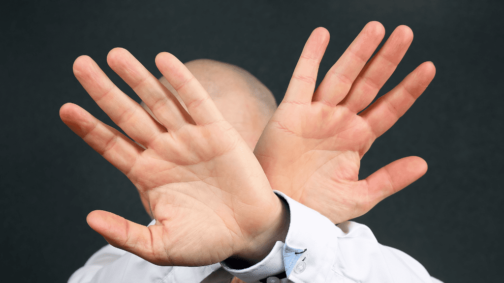 Zwei Hände die sich vor einem Gesicht kreuzen.